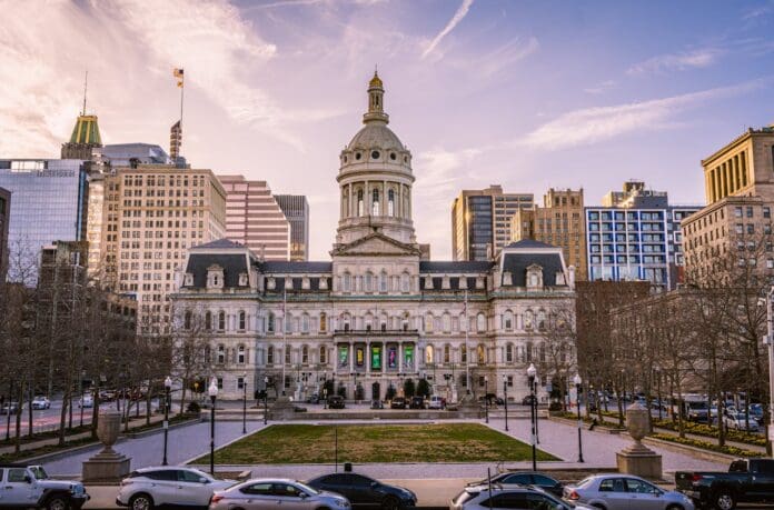 Historical building of Baltimore City Hall in Maryland, light blue sky and cars